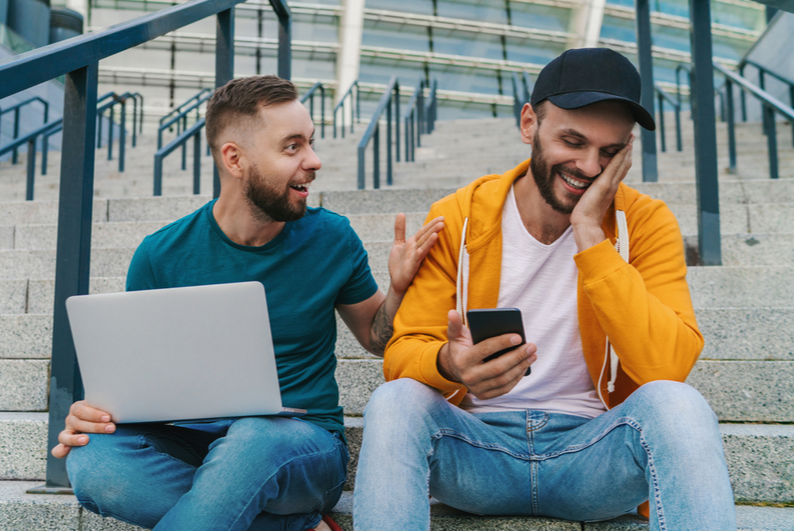 Friends betting on a smartphone and laptop outside a stadium