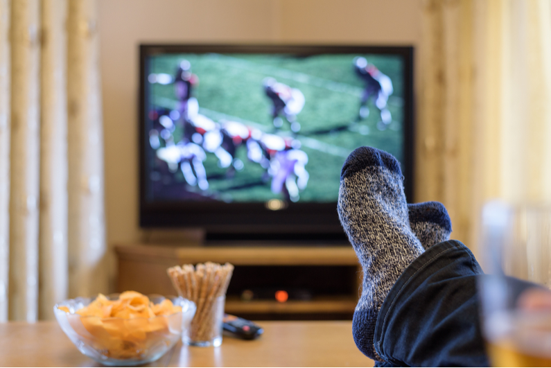 Person with their feet on a coffee table and football on TV in the background