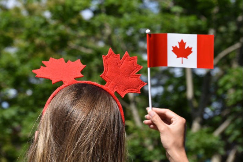 Woman wearing a red maple leaf headband and holding small Canadian flag