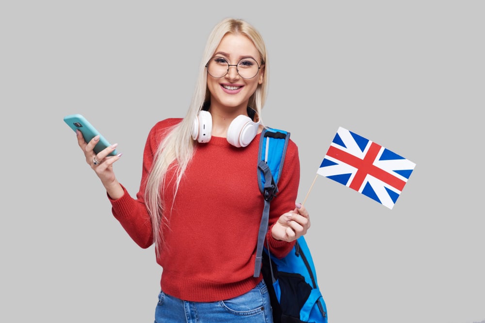 blonde woman with glasses holds a mobile phone in one hand and the Union Jack flag in the other