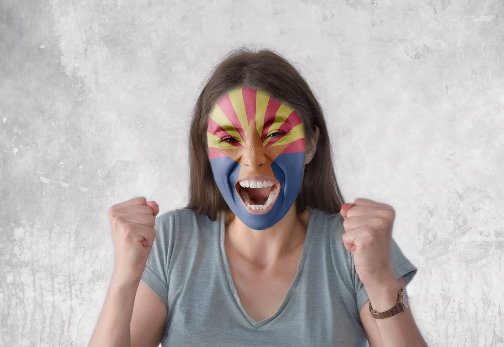 Woman with Arizona flag painted on her face happily clenching her fists