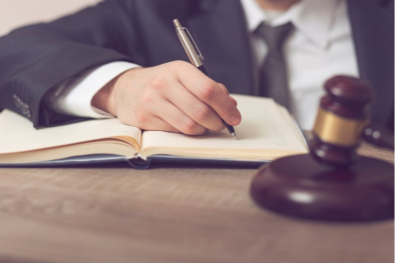 hand signing legislative document with a pen, judge's mallet in the foreground