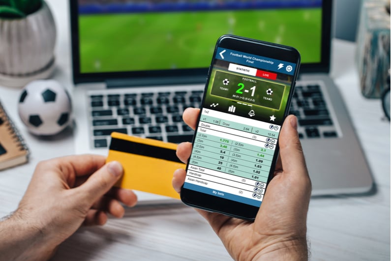 Man holding a smartphone and credit card for betting on sports