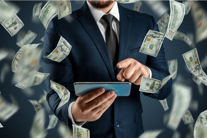 Man in suit betting on mobile phone surrounded by flying $100 bills