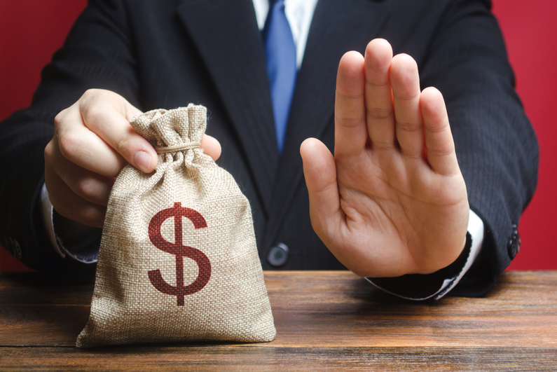 Man holding a moneybag on a table and issuing a "stop" signal with his other hand