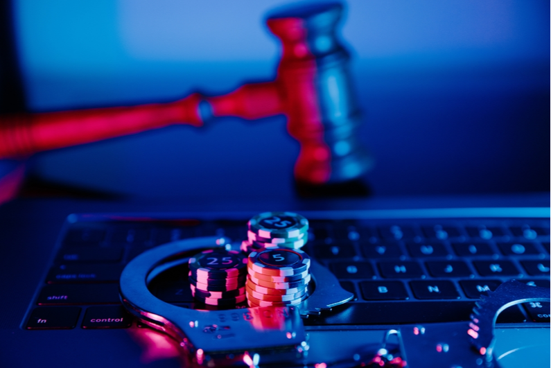 Poker chips and handcuffs on a laptop with a gavel in the background