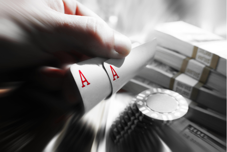 Black and white photo of pocket Aces with chips and cash in the background