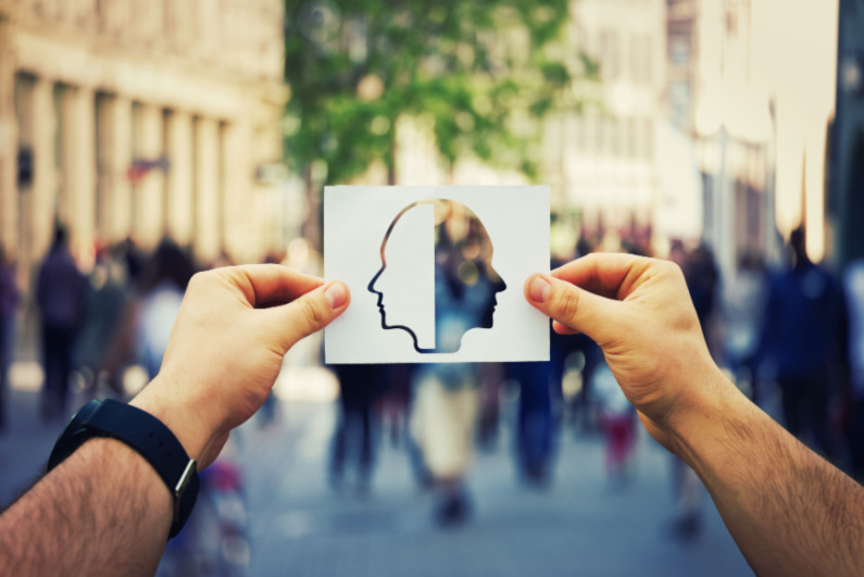 Man holding paper sheet with two faced head to convey bipolar disorder