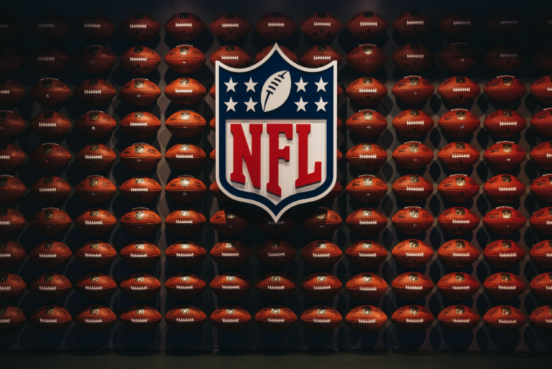 NFL logo in front of a wall of footballs