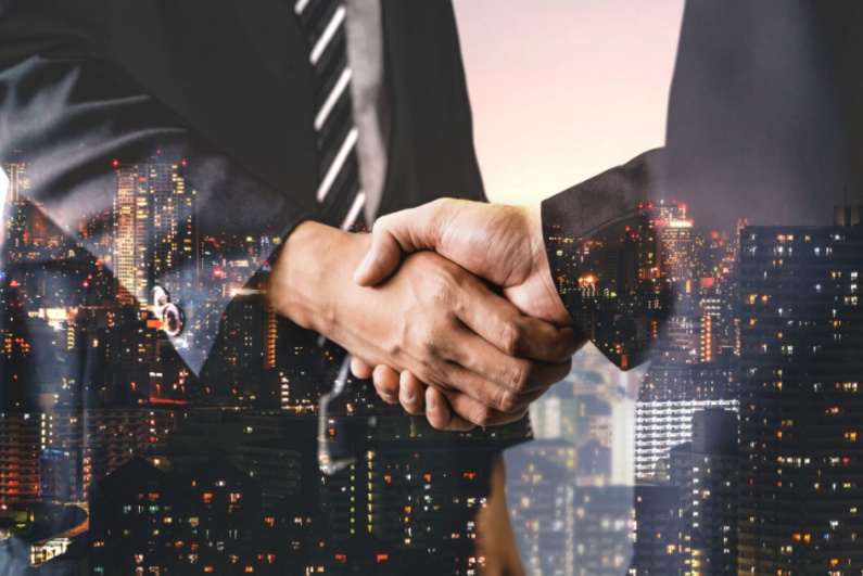 Business people shake hands with the city skyline in the background