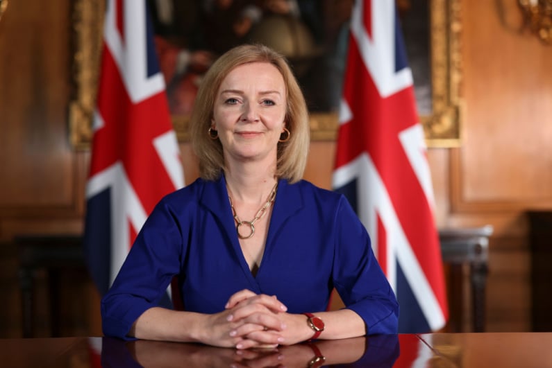 Liz Truss sitting in front of Union Jack flags