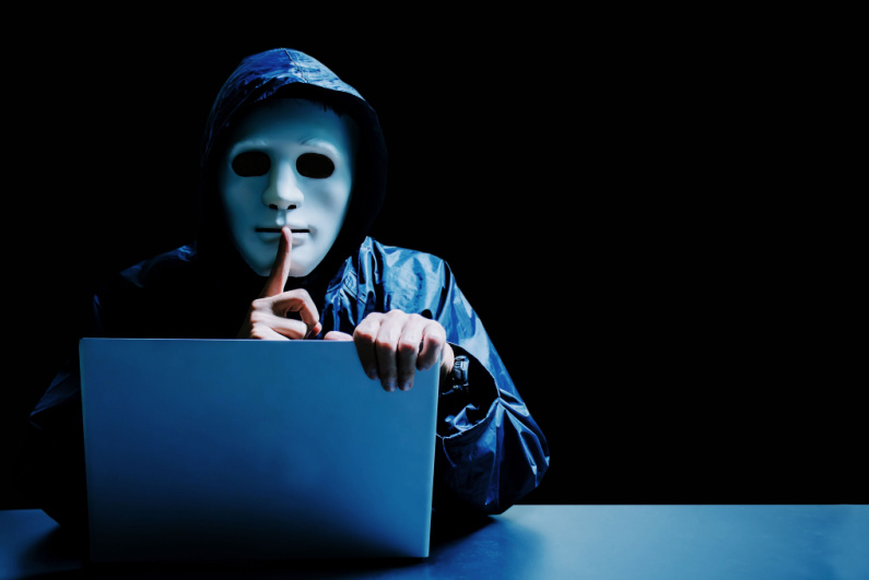 A hacker wearing a white mask sitting at a laptop
