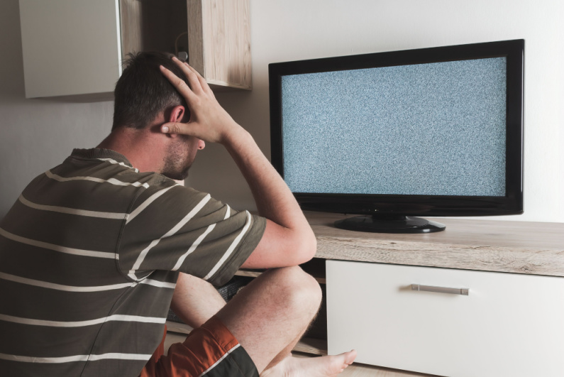 Man holding his head watching TV