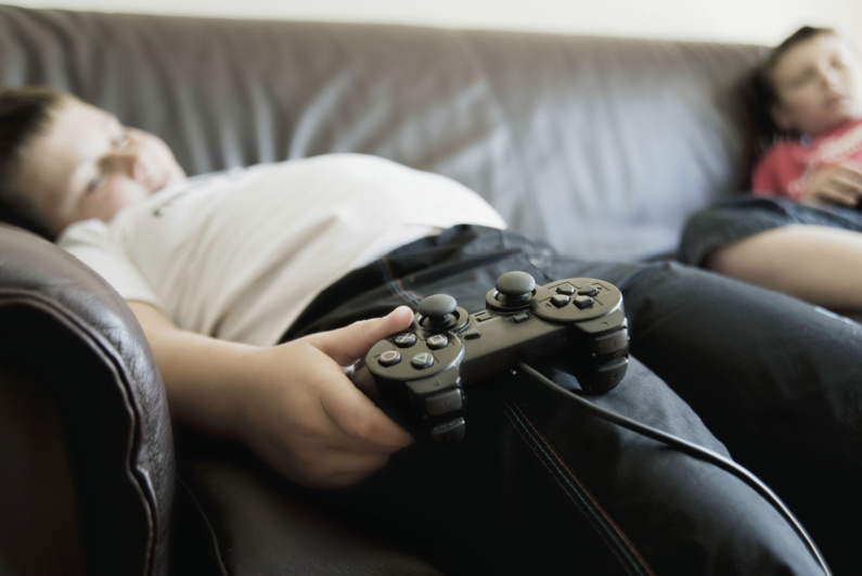 Dua anak laki-laki tertidur di sofa, memegang pengontrol video game.