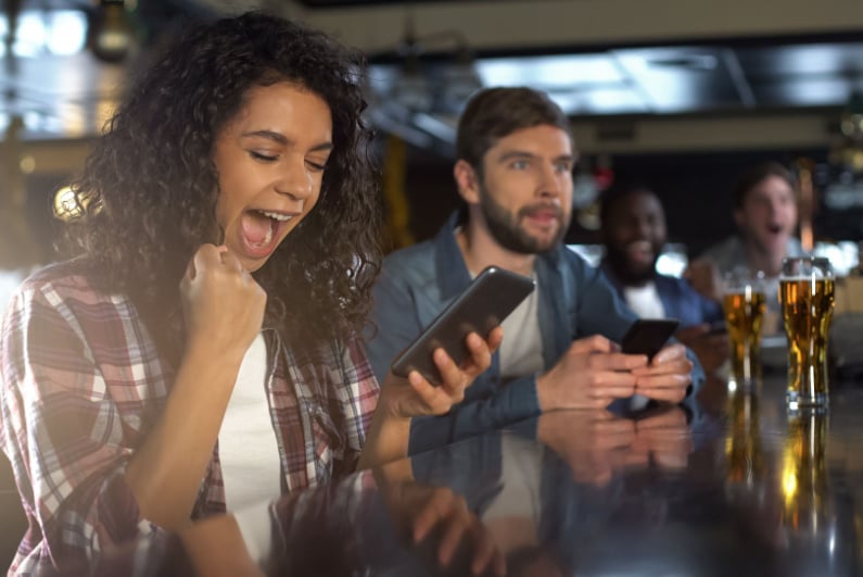 Woman looking at her phone and celebrating in a sports bar