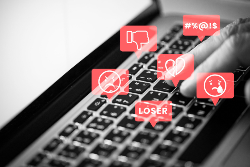 Person typing with negative emojis emanating from keyboard, cyberbullying concept