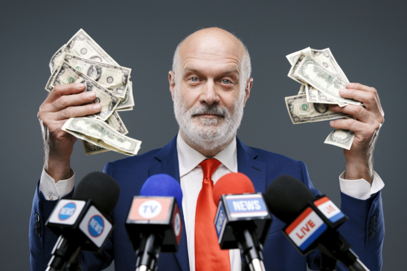 Politician standing at microphones holding money