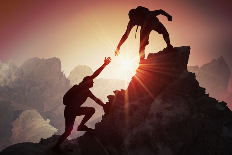 Rock climber extending a hand to help another