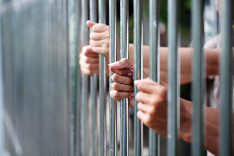 Two pairs of hands behind bars