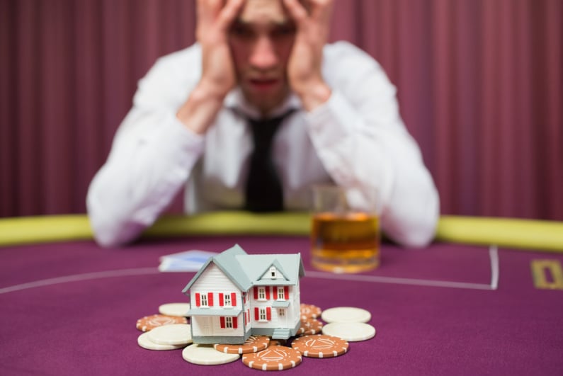 Man losing pot, which includes a model of a house, in a poker game