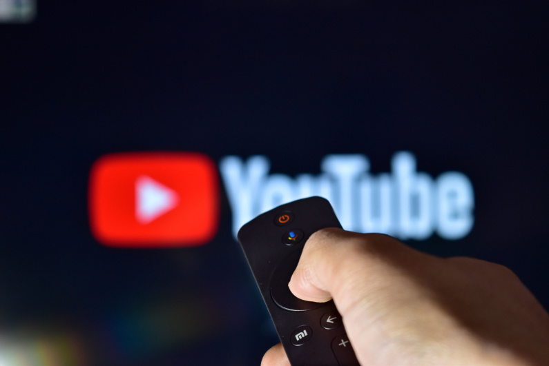 Person using remote control with YouTube logo on TV in background