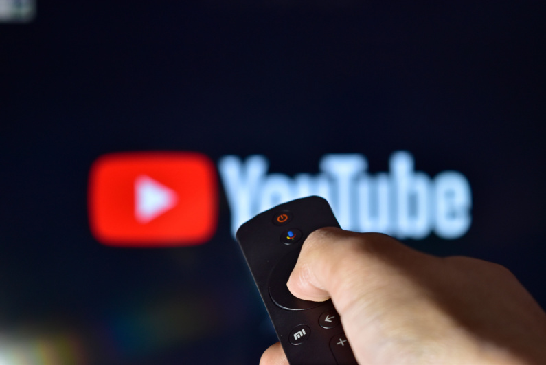 Arka planda TV'de YouTube logosu bulunan uzaktan kumandayı kullanan kişi