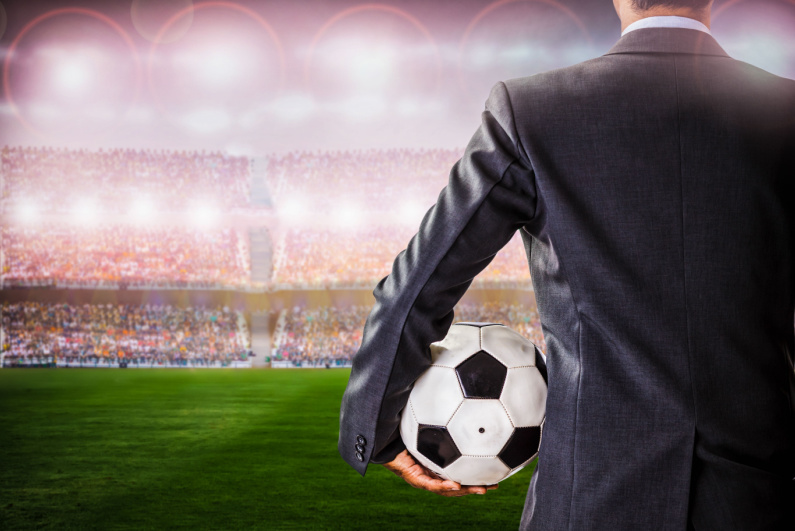 Man in suit holding soccer ball looking out over the pitch