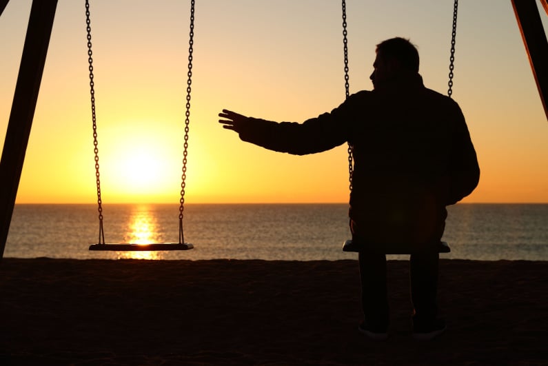 Man alone on a swing on the beach in winter