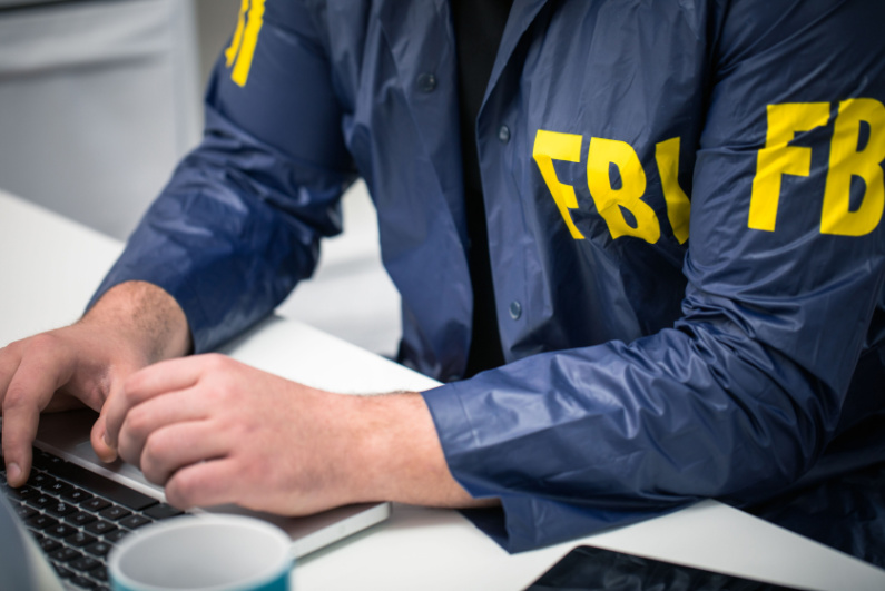 Man in FBI windbreaker at laptop