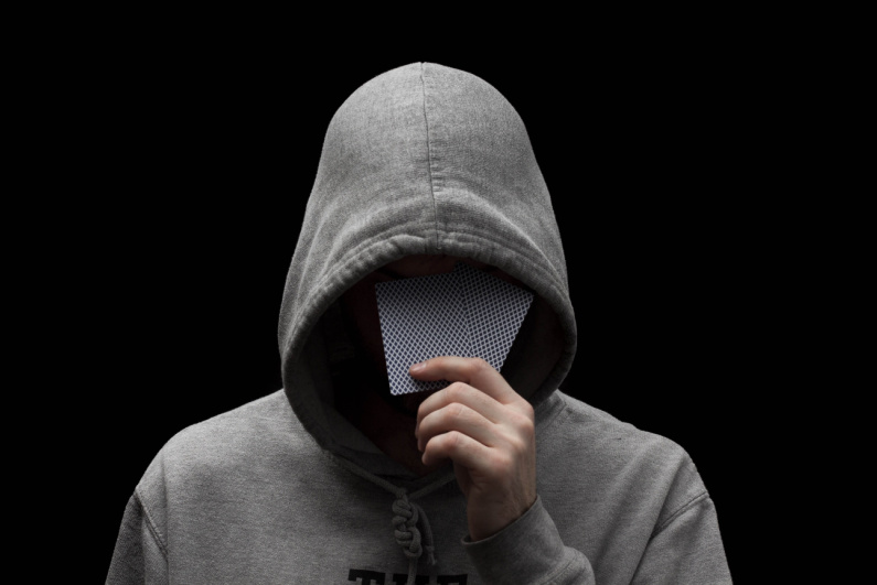 Mysterious man in hoodie hiding face with hole cards