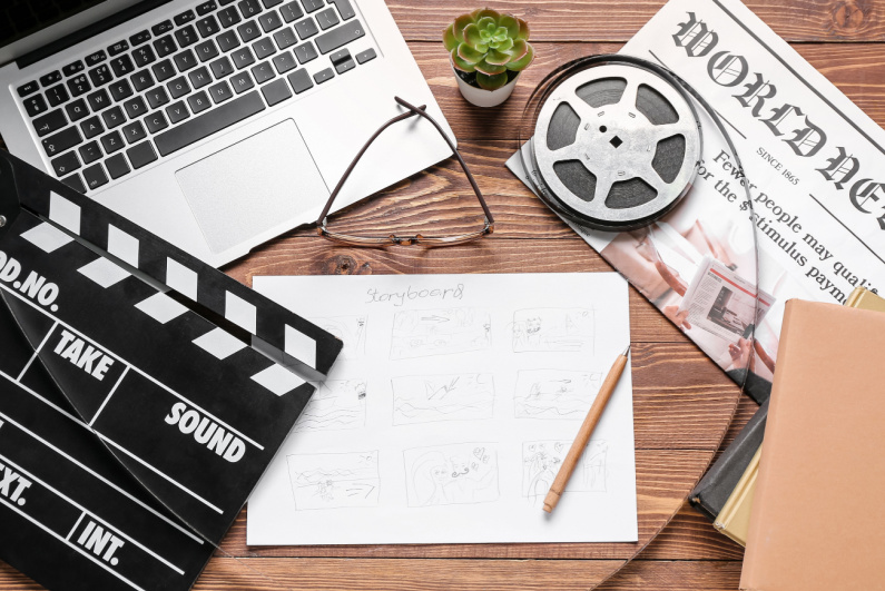 A movie clapper, a laptop, glasses, and a film reel on a table