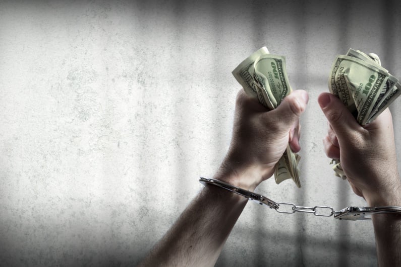 Handcuffed hands grasping wads of cash