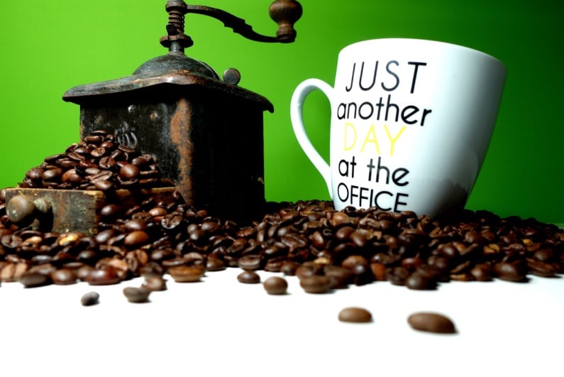 Old fashioned coffee grinder and mug that says JUST ANOTHER DAY AT THE OFFICE