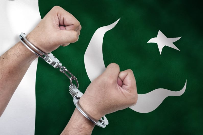 Man in handcuffs in front of Pakistan flag