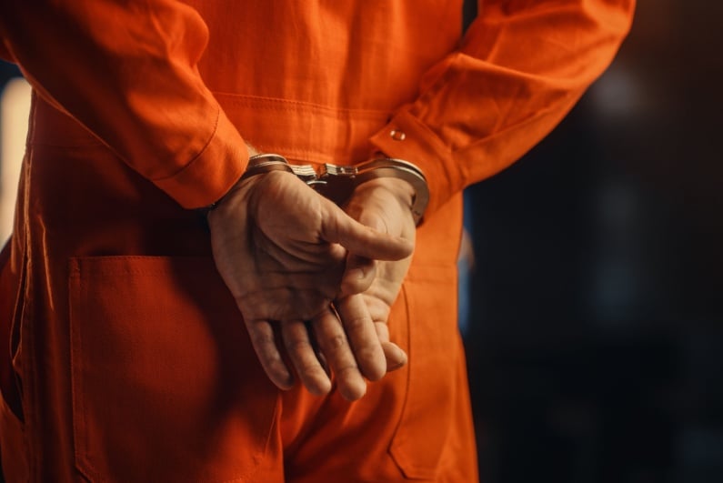 Man in orange jumpsuit handcuffed