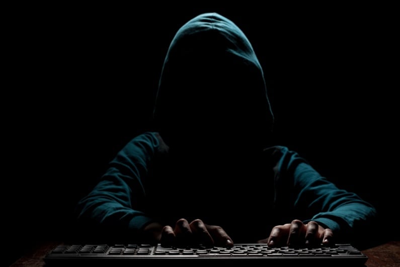Hooded man typing in darkness