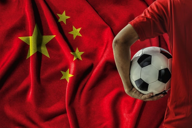 Man holding soccer ball in front of Chinese flag