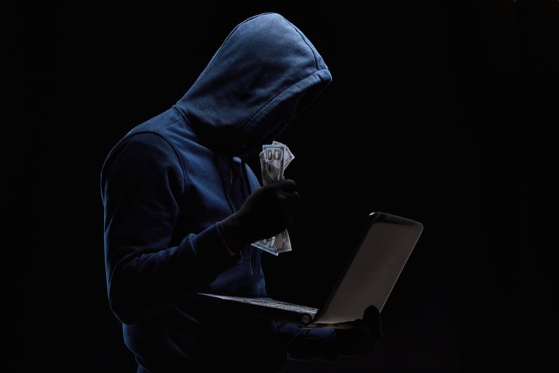 Hooded hacker clutching cash