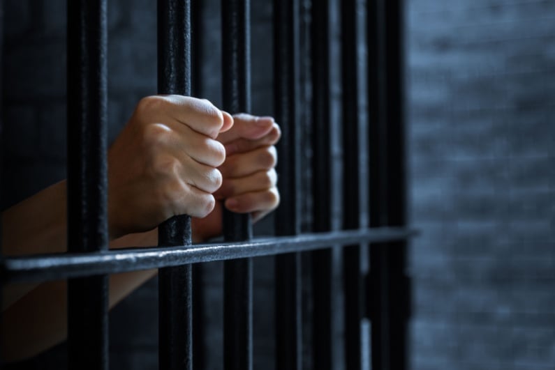 Person holding bars of jail cell